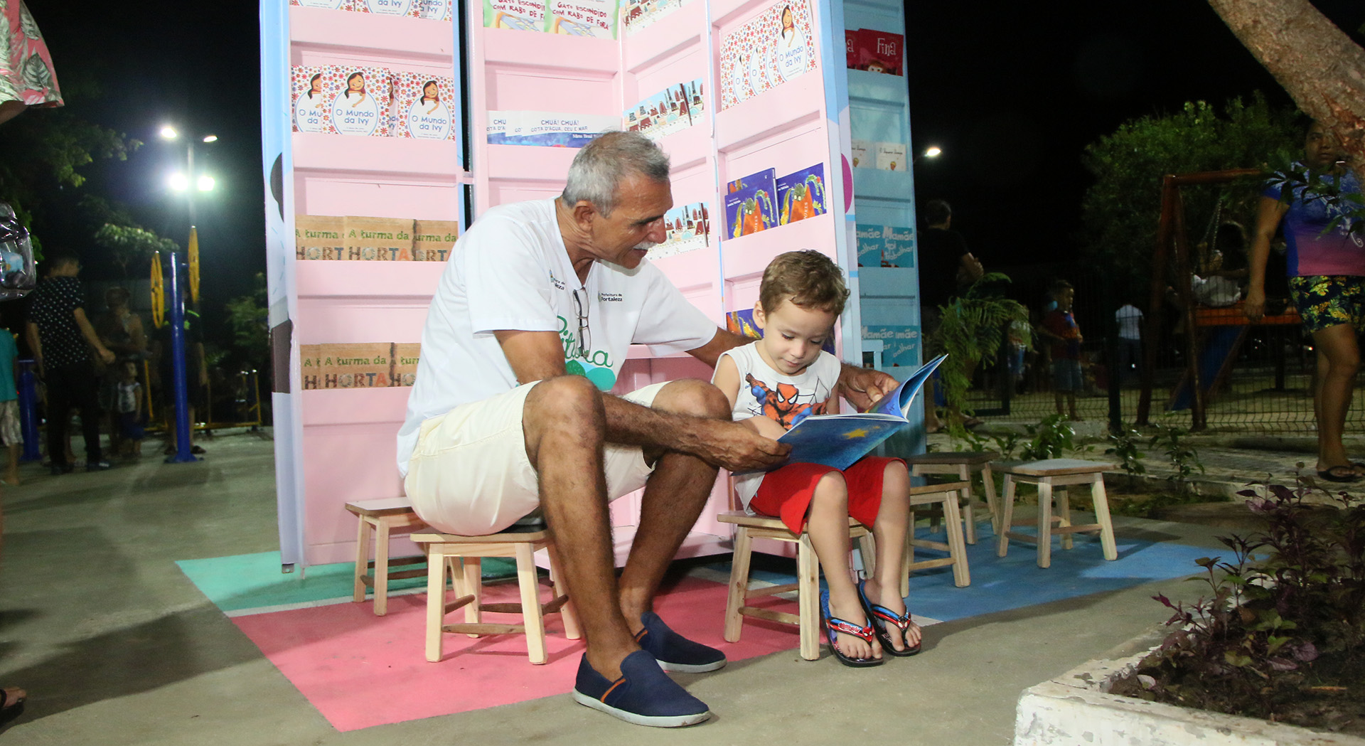 senhor sentado ao lado de garoto lendo livro com quiosque de livros ao fundo